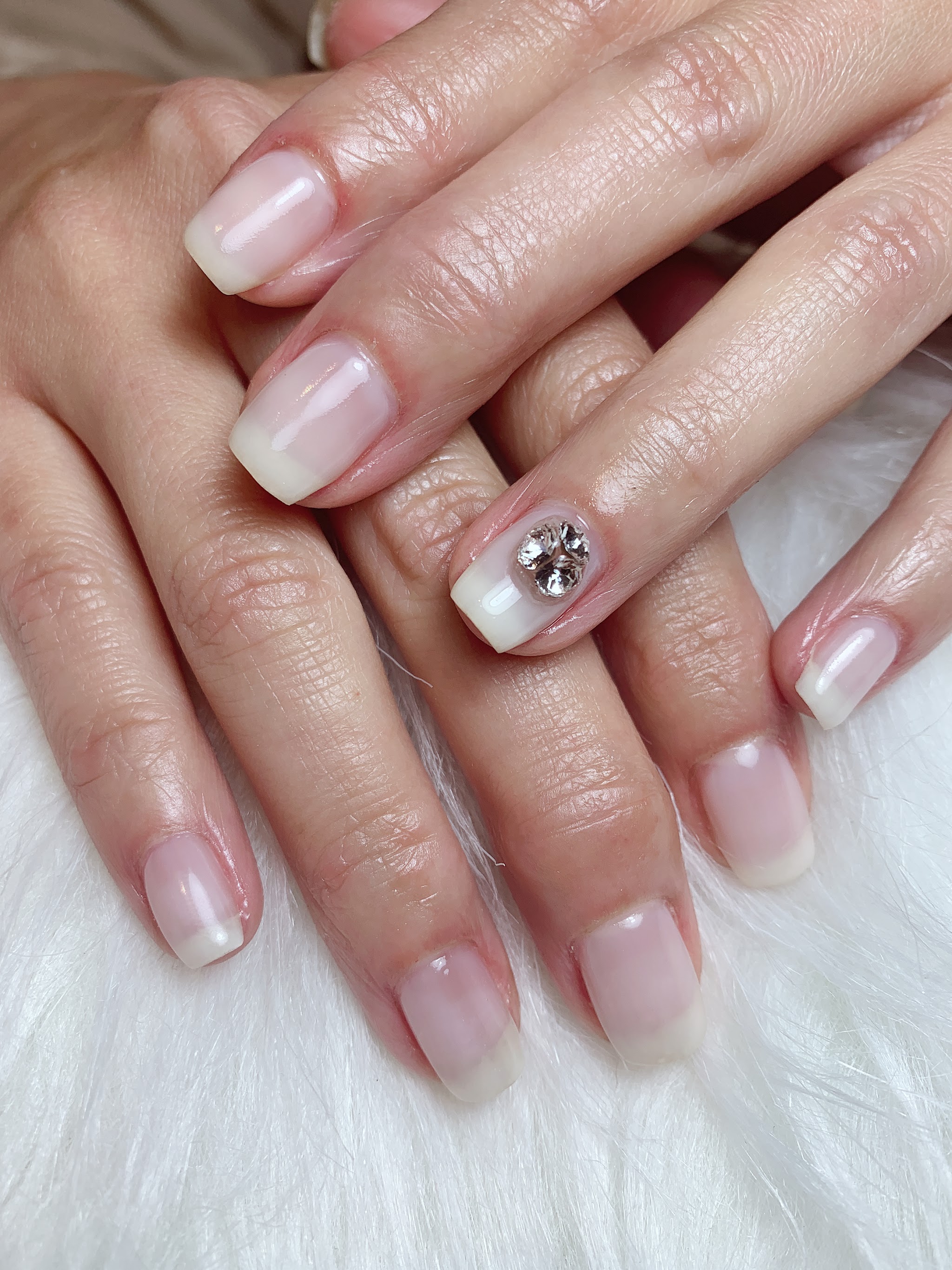 Natuurlijke nude gelnagels met één kristal, op wit bont